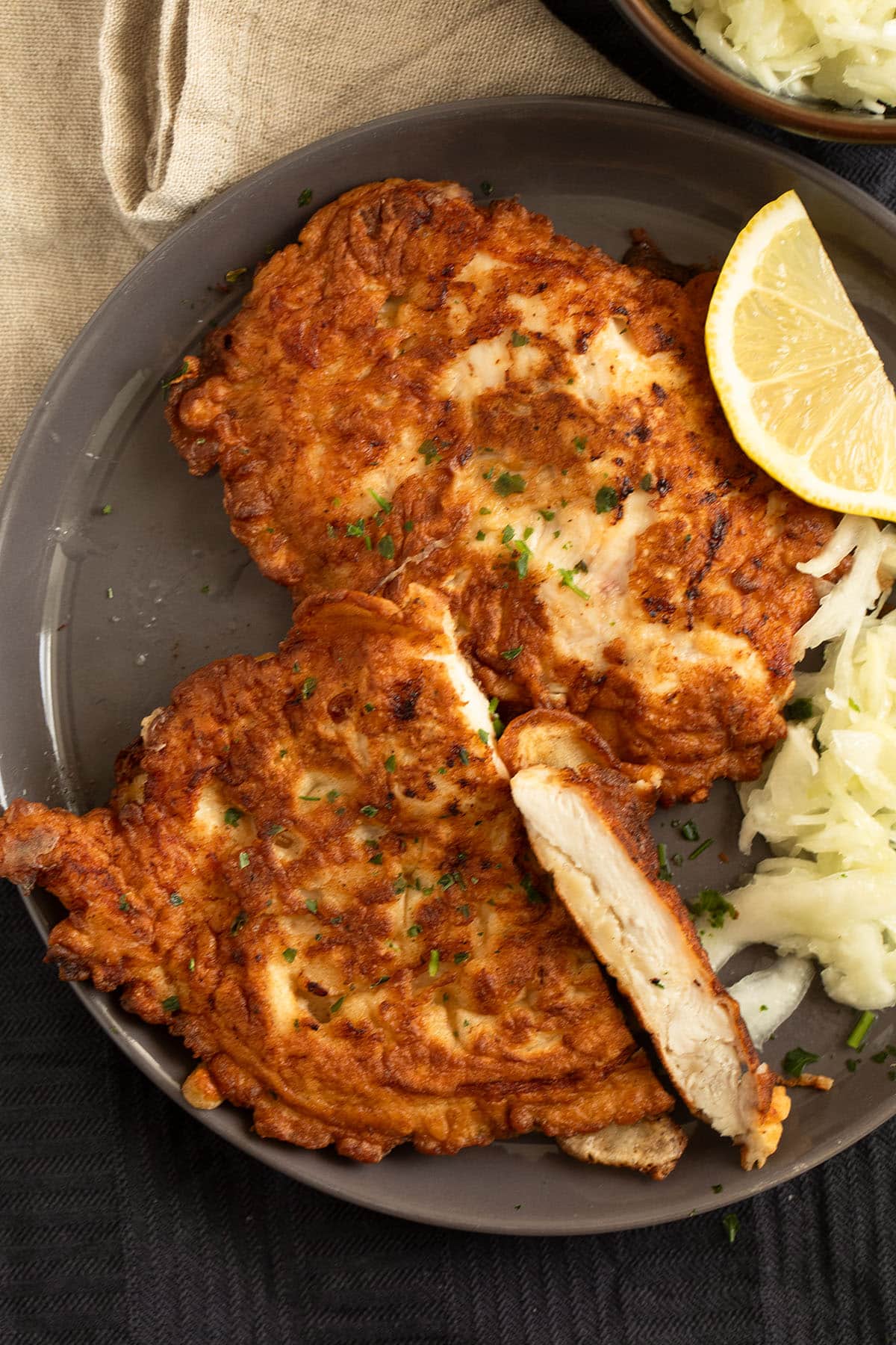 two golden fried chicken pieces in pancake batter on a plate with a slice of lemon.