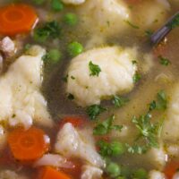 close up of soup with dumplings, carrots and peas