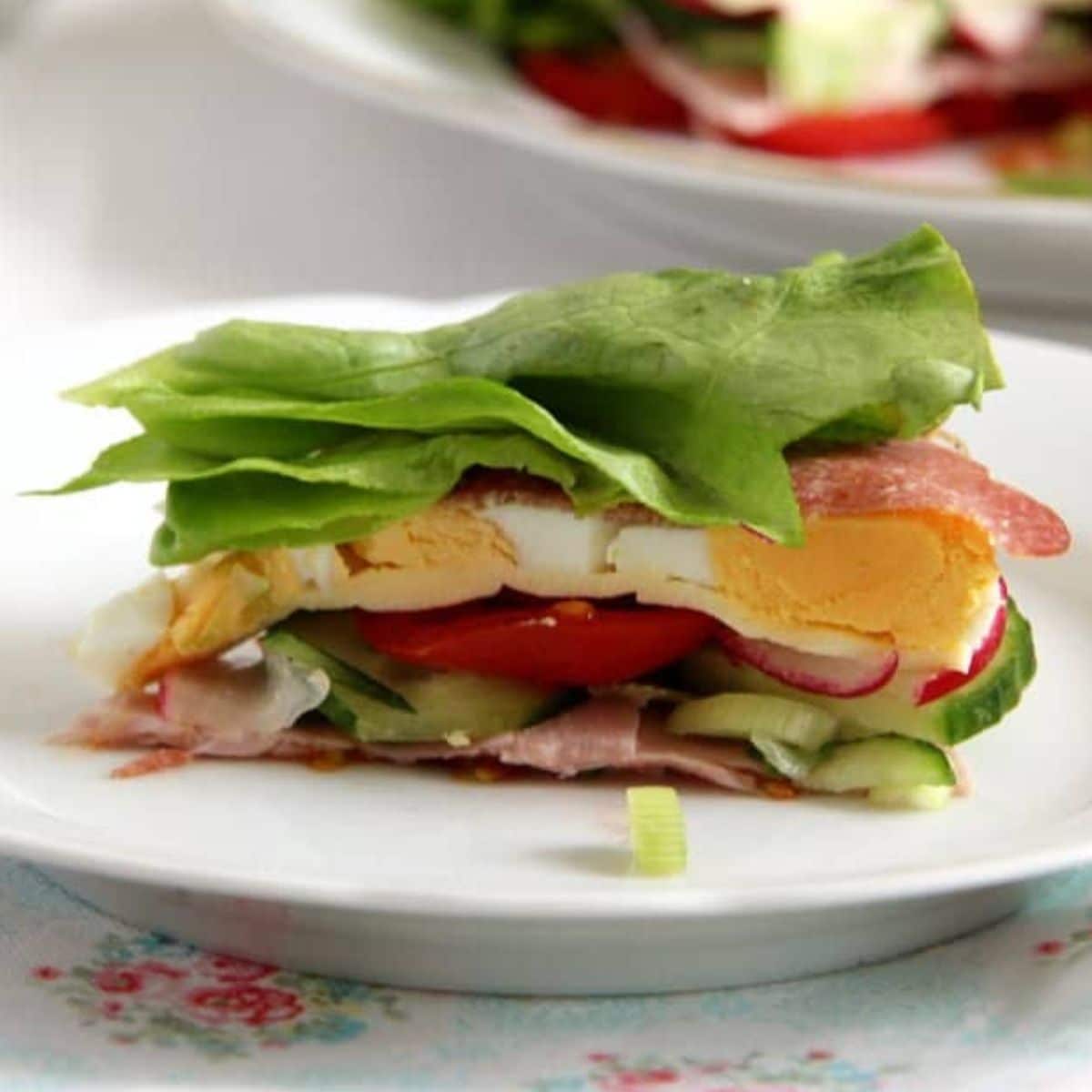 salad cake with layers of lettuce, tomatoes, deli meats, cheese slices and hard-boiled eggs on a small plate.