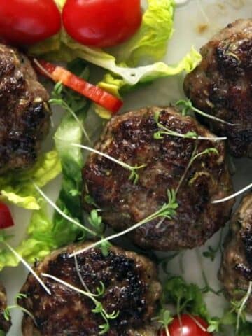 juicy zucchini meatballs with salad leaves and small tomatoes on the side.