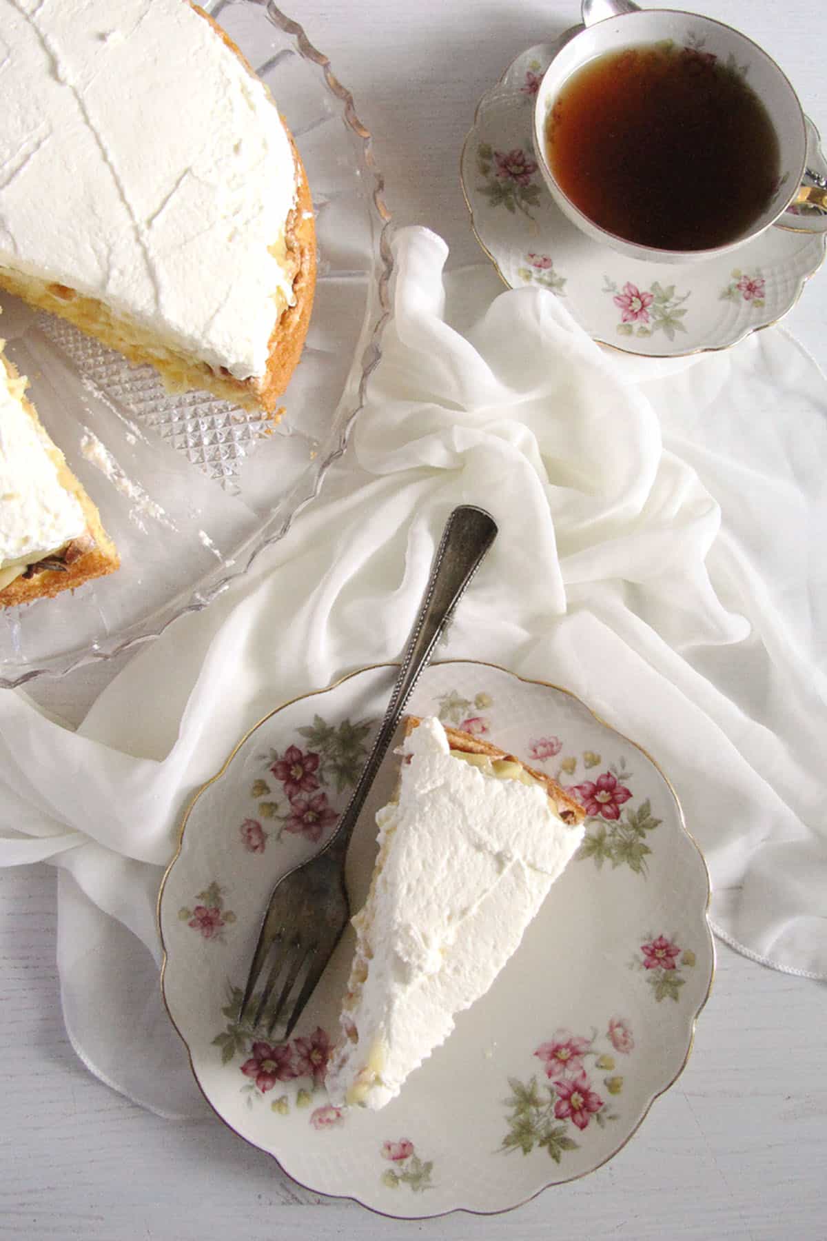 one slice of german apple cake on a vintage cake, the res t of the cake on platter, a cup of coffee.