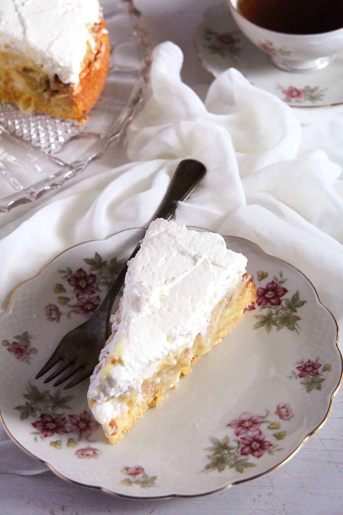 a slice of apple cake topped with whipped cream on a vintage plate with flowers on it. 