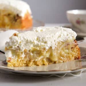 a slice of german apple cream cake covered with whipped cream.