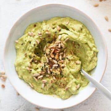 spicy avocado spread for bread sprinkled with sunflower seeds and spices in a bowl.