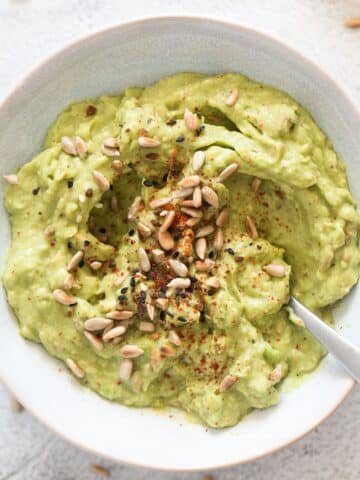 spicy avocado spread for bread sprinkled with sunflower seeds and spices in a bowl.