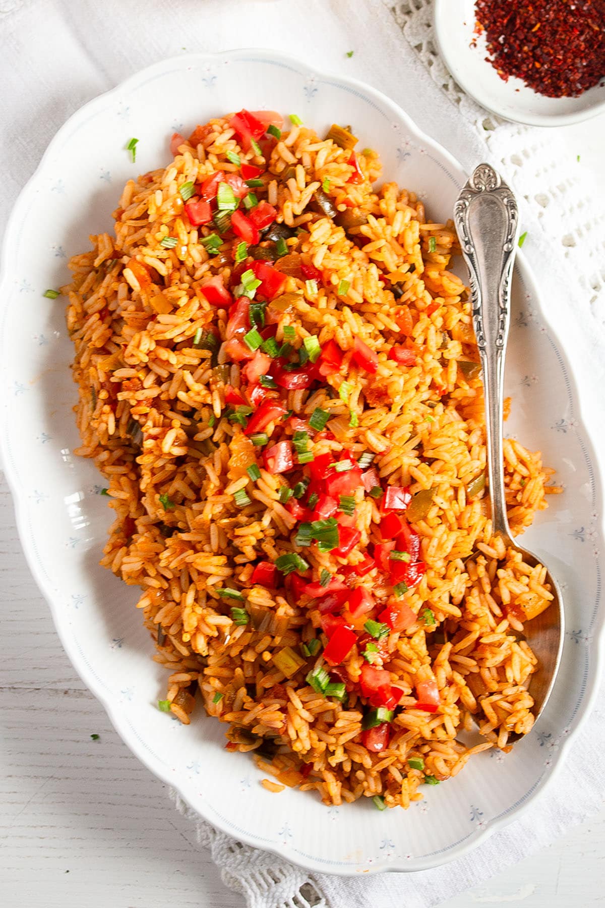 a platter full of orange-colored bbq rice topped with diced tomatoes and parsley.