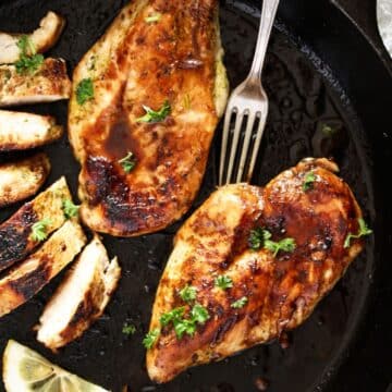 cast-iron chicken breast in the pan, a fork and a sliced piece of breast.