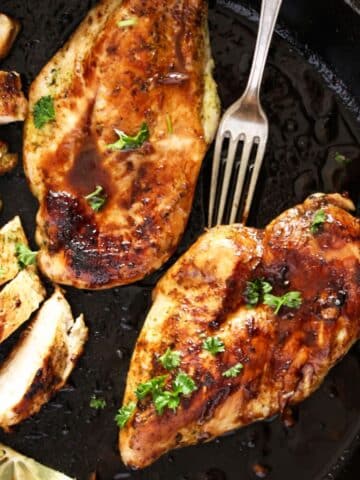 cast-iron chicken breast in the pan, a fork and a sliced piece of breast.