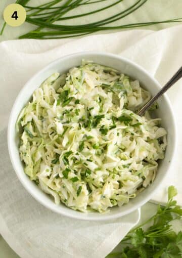 german coleslaw with lots of herbs in a white bowl with a spoon in it.