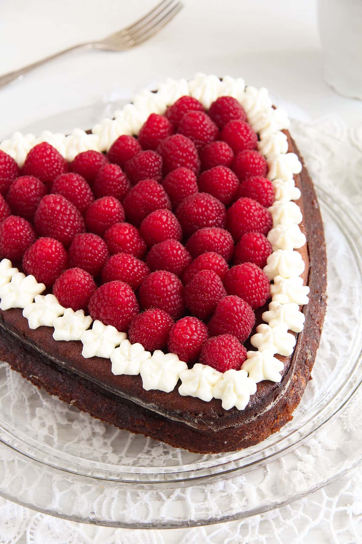 cheesecake in the shape of a heart with fresh raspberries and whipped cream on top.