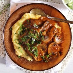 mushrooms stew served over creamy polenta in a brown bowl.