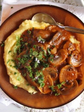 mushrooms stew served over creamy polenta in a brown bowl.