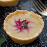mini raspberry tartlet with white chocolate and raspberry coulis filling decorated with mint leaves.
