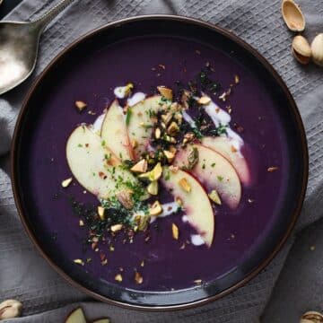 bowl of red cabbage soup garnished with apple slices and chopped pistachios.
