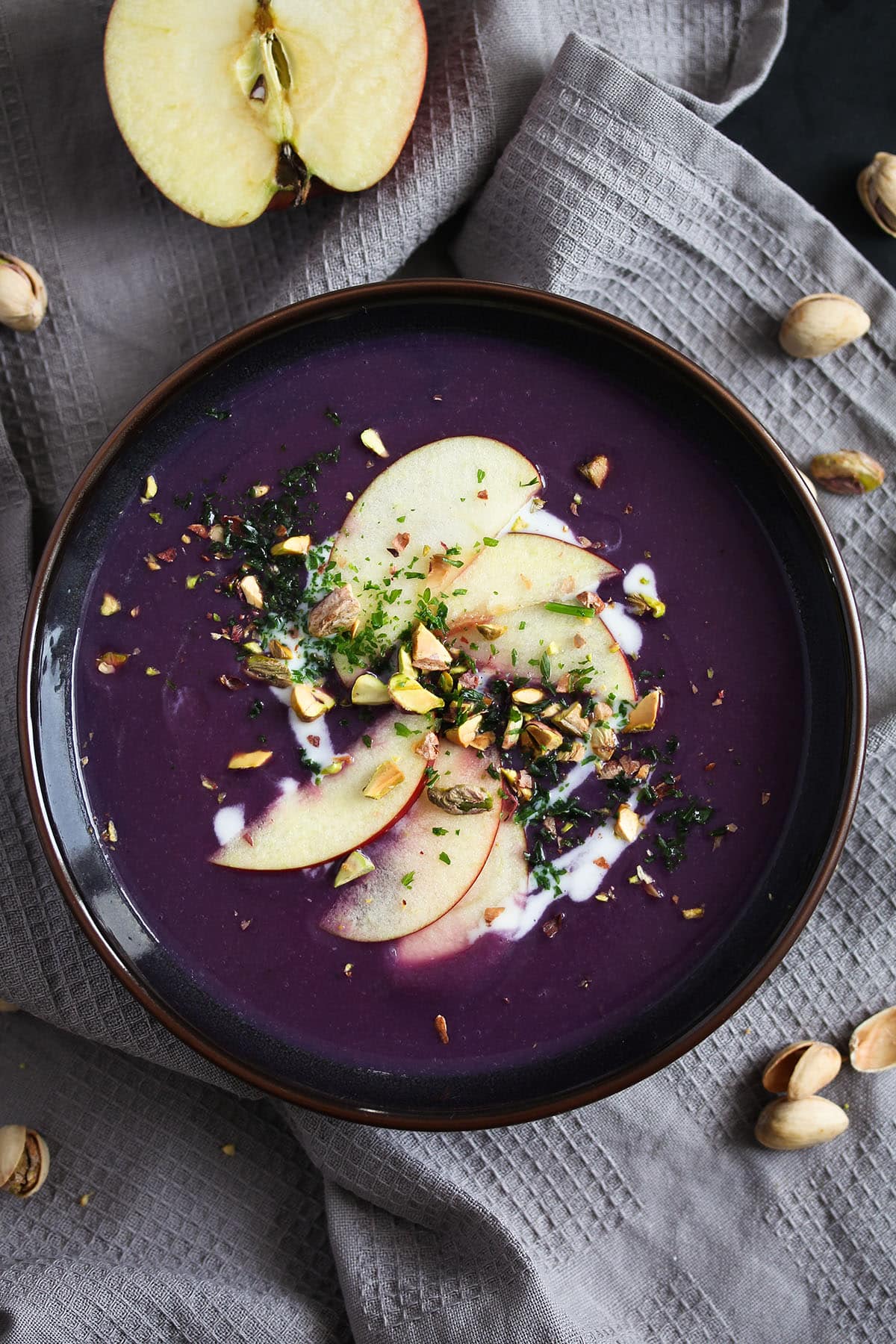 soup with red cabbage in a bowl, half an apple on the side.