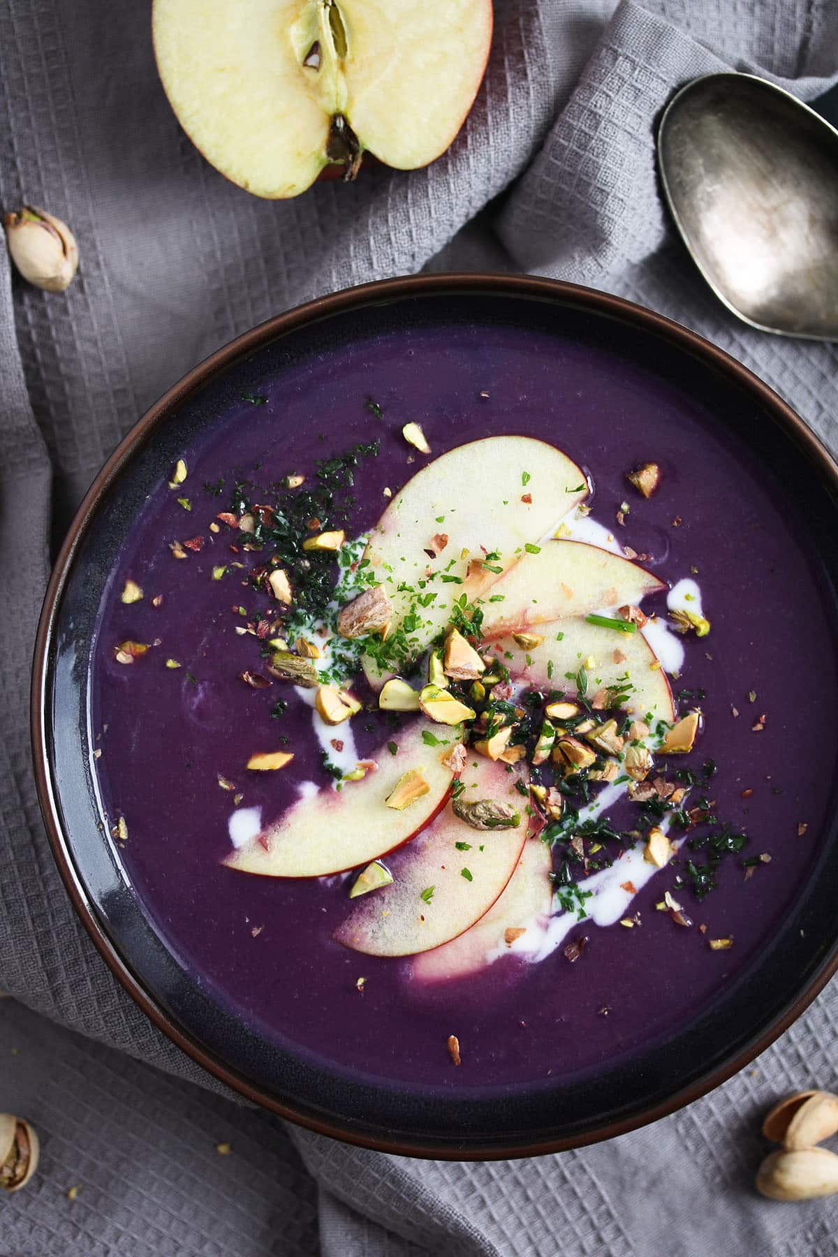 bowl of purple cabbage soup topped with apple slices and pistachios.