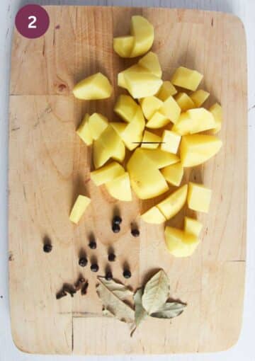 chopped potatoes, juniper berries, cloves and bay leaves on a wooden board.