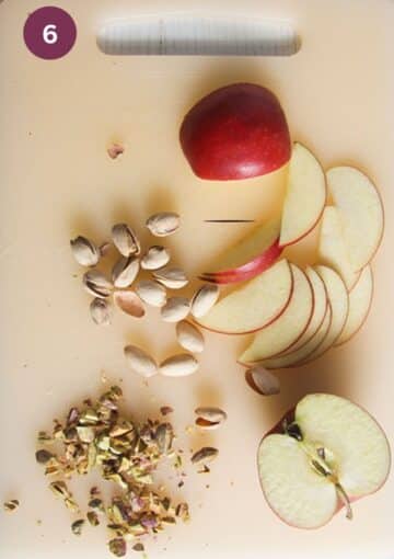 shelled and chopped pistachios, a apple half and apple slices on a cutting board.