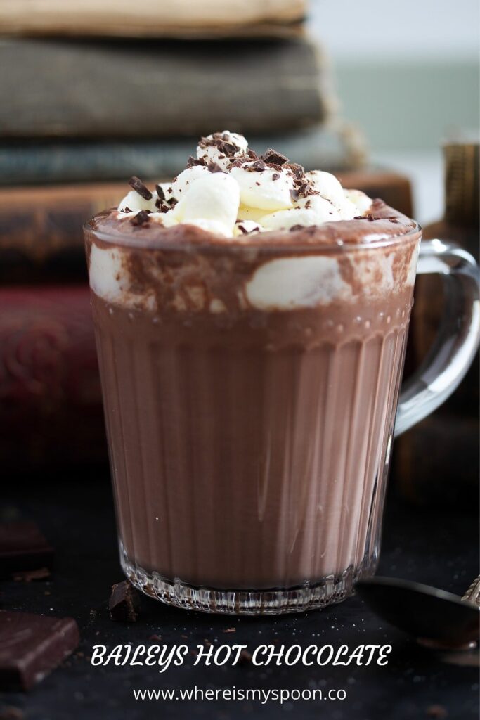 cup with chocolate topped with cream and chocolate shavings with old books behind