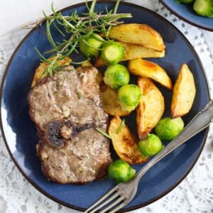 baked lamb chops and potatoes with brussels sprouts and rosemary on a plate with a fork.