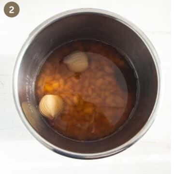 cooked beans and one halved onion in a pot.