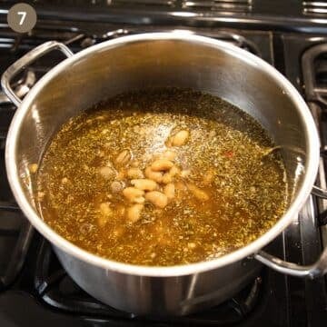 adding beans and herbs to a bot of cooking bone broth soup.