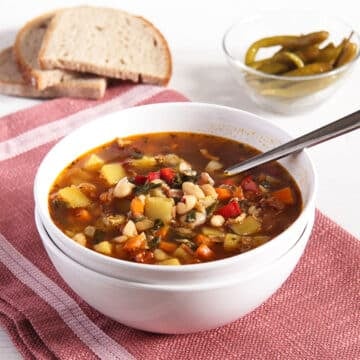 bone broth vegetable broth in a bowl, slices of bread and green chili peppers behind it.