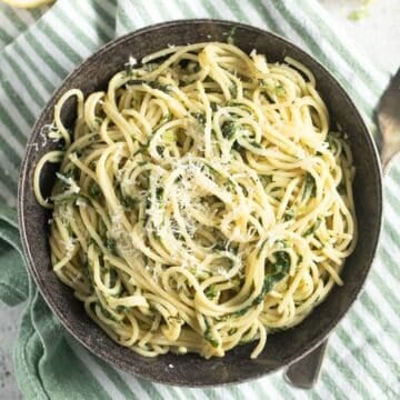 a bowl of frozen spinach pasta sprinkled with parmesan on a striped kitchen cloth.