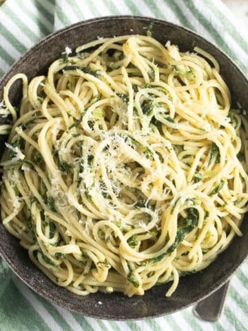 a bowl of frozen spinach pasta sprinkled with parmesan on a striped kitchen cloth.