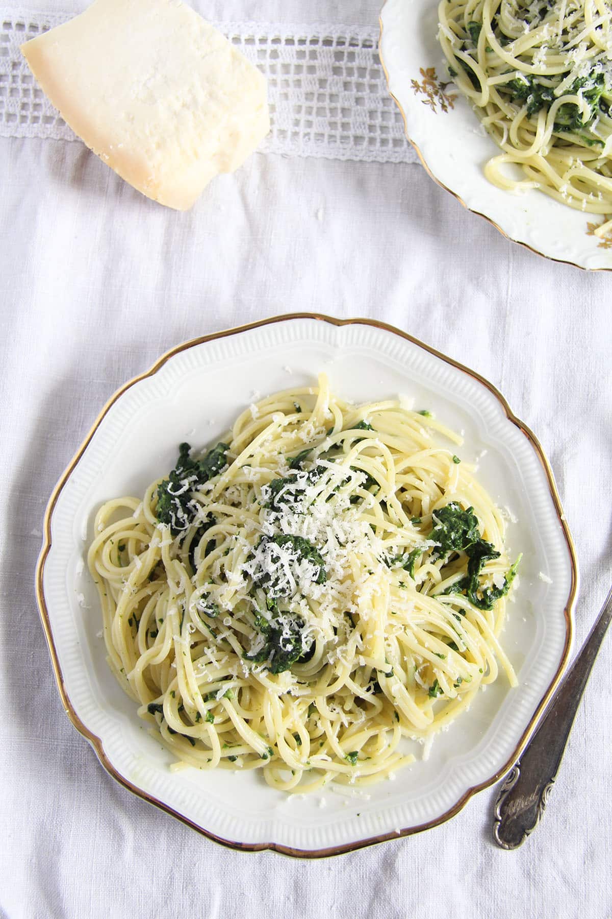 spaghetti with spinach on a plate and a piece of parmesan near it.