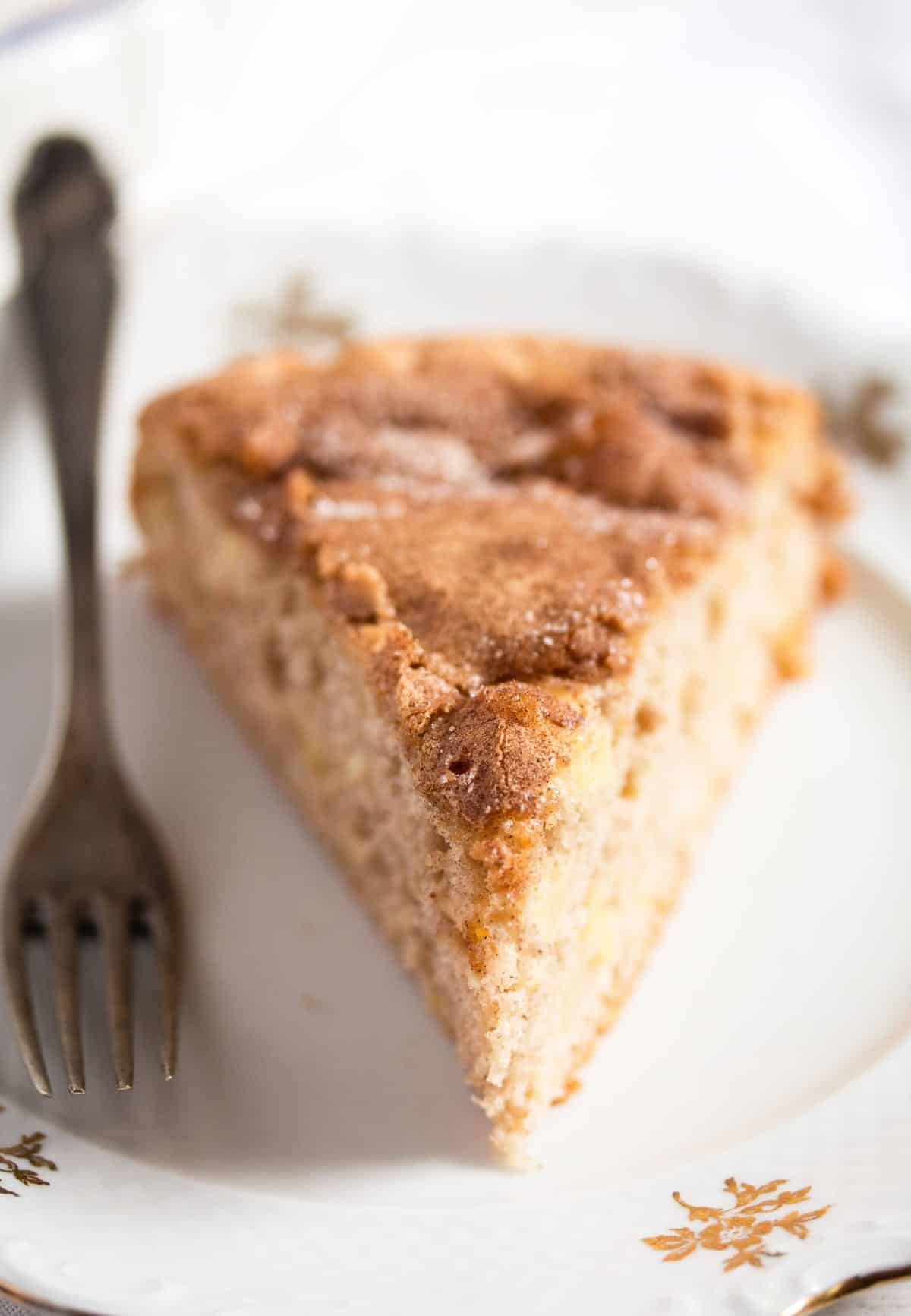 slice of apple cake sprinkled with sugar on a small plate with a fork.