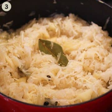 cooking sauerkraut with apples in a pot, a bay leaf sticking out.