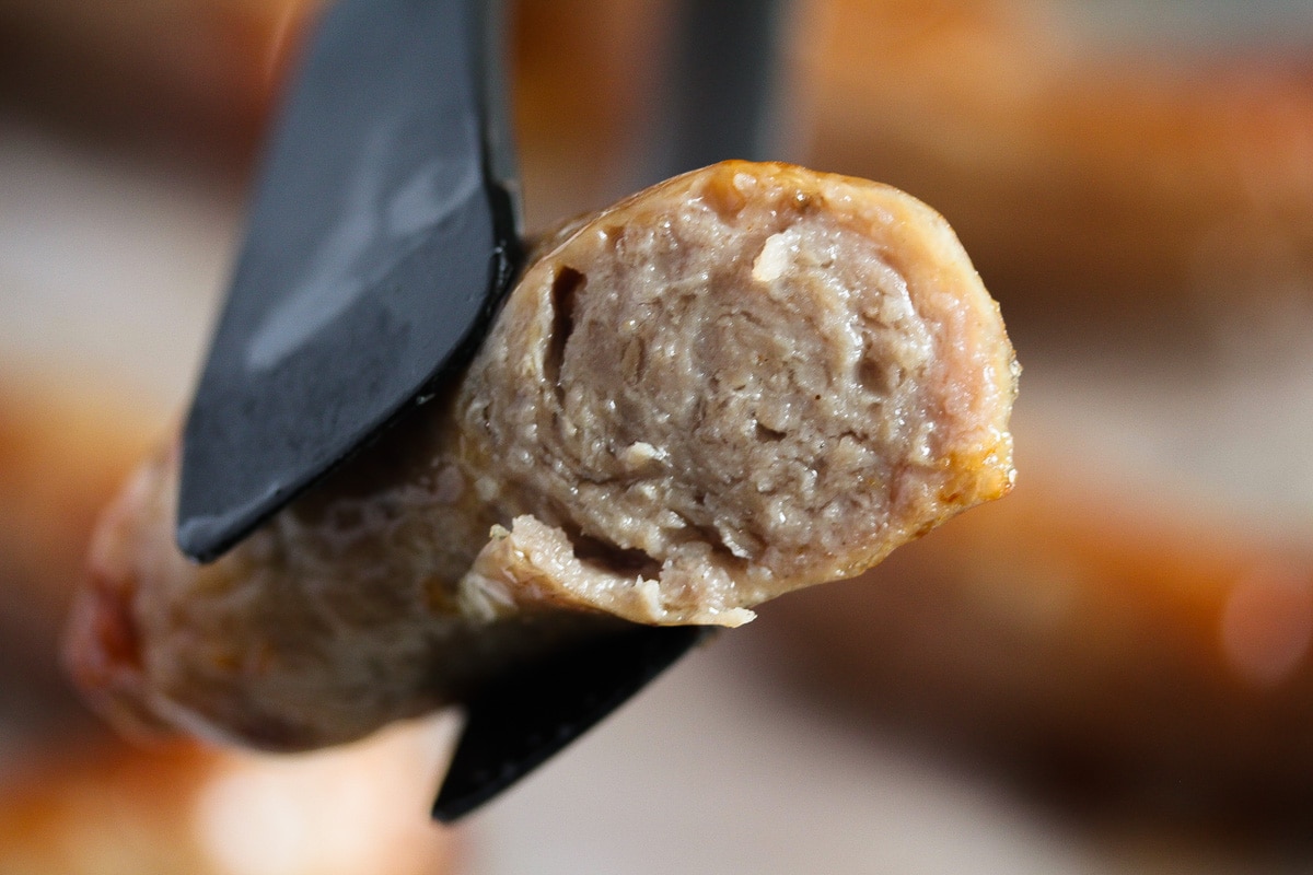 half a cooked sausage held with tongs