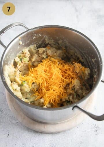 adding grated cheddar cheese to mashed potatoes in a pot.