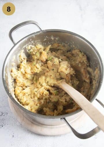 stirring mashed cabbage and potatoes with a wooden spoon in a pot.