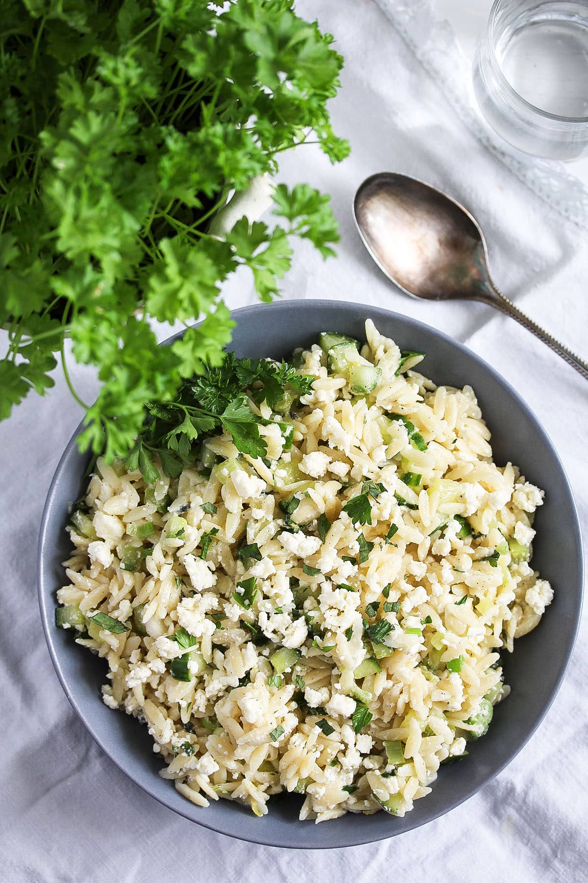 lemon orzo salad with feta and cucumbers in a bowl, a spoon near it.