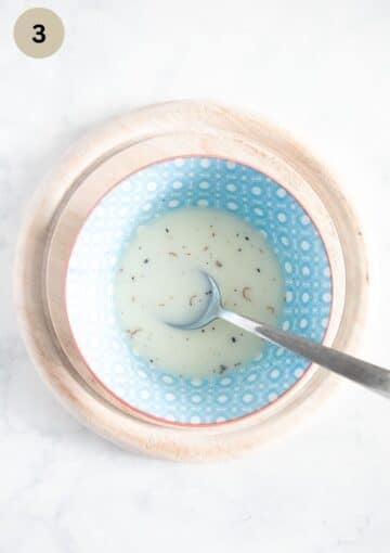 milk, vanilla seeds, and sugar mixture for adding to flour to make yeast dough in a bowl with a spoon in it.