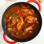 close up of a red dutch oven with rabbit stew sprinkled with parsley.