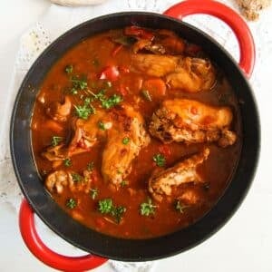 close up of a red dutch oven with rabbit stew sprinkled with parsley.