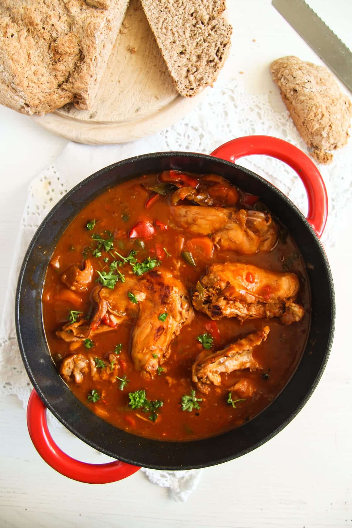 overhead view of a pot with stewed rabbit in red sauce served with rustic bread.