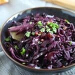 a bowl full of red cabbage with red wine sprinkled with fresh parsley.