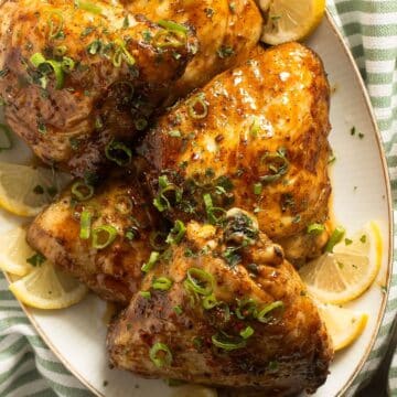 four sweet and sour chicken thighs served with lemon wedges on a platter.