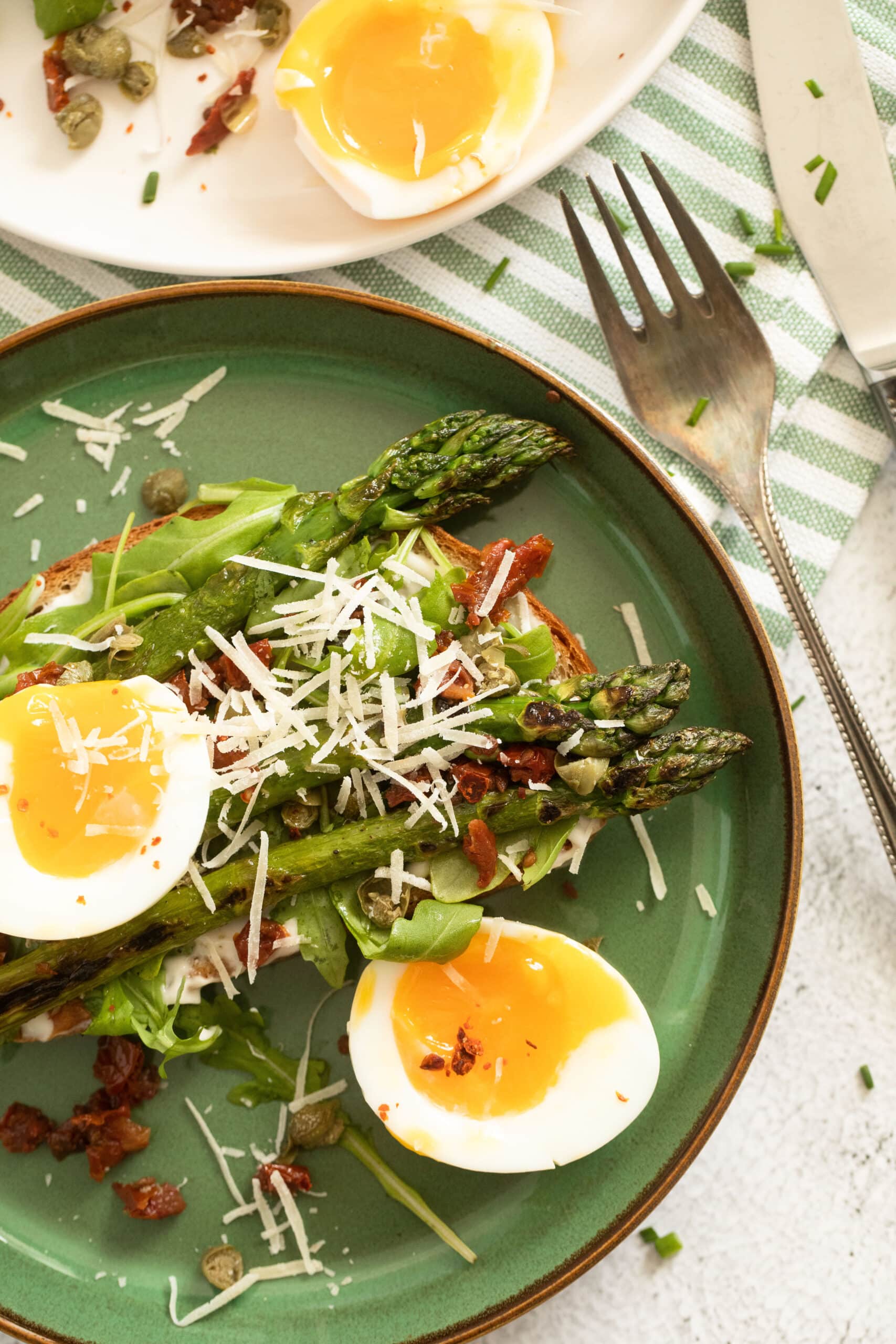 asparagus and eggs with sun-dried tomatoes and parmesan on a green plate.