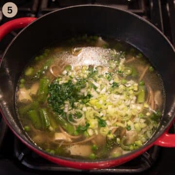 adding green onions to asparagus chicken soup on the stove.