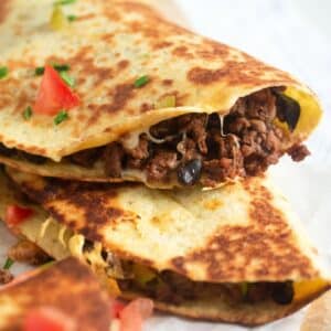 close up ground beef quesadillas sprinkled with chopped tomatoes.