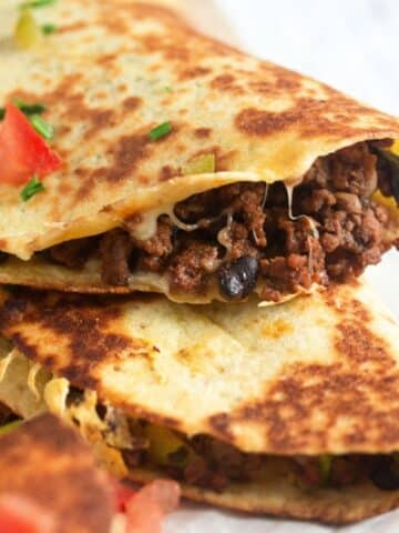 close up ground beef quesadillas sprinkled with chopped tomatoes.