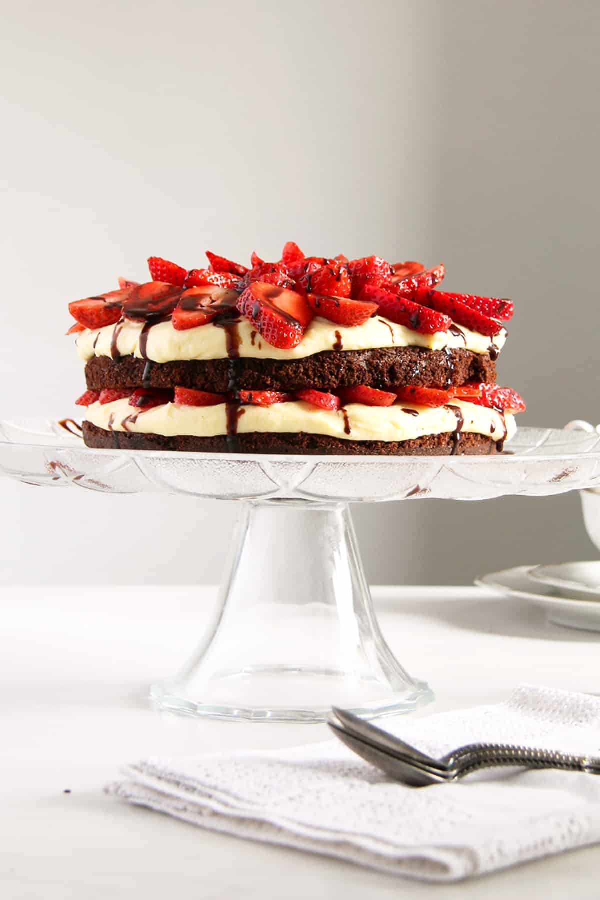brownie strawberry cake drizzled wiht chocolate on a cake platter. 