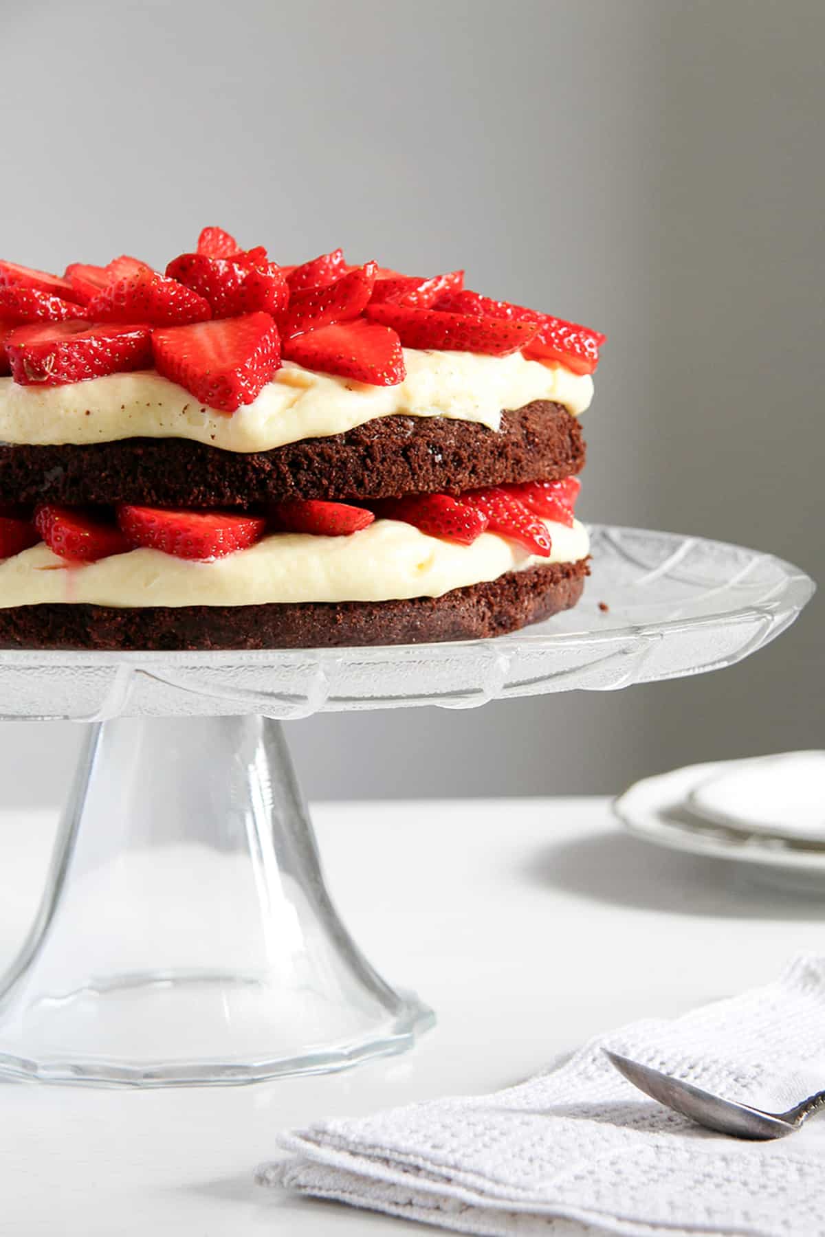 one brownie strawberry cake with layers of strawberries and filling on a tall platter.