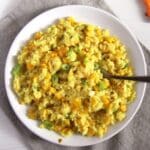 cheesy corn rice with vegetables on a small plate with a fork sticking into it.