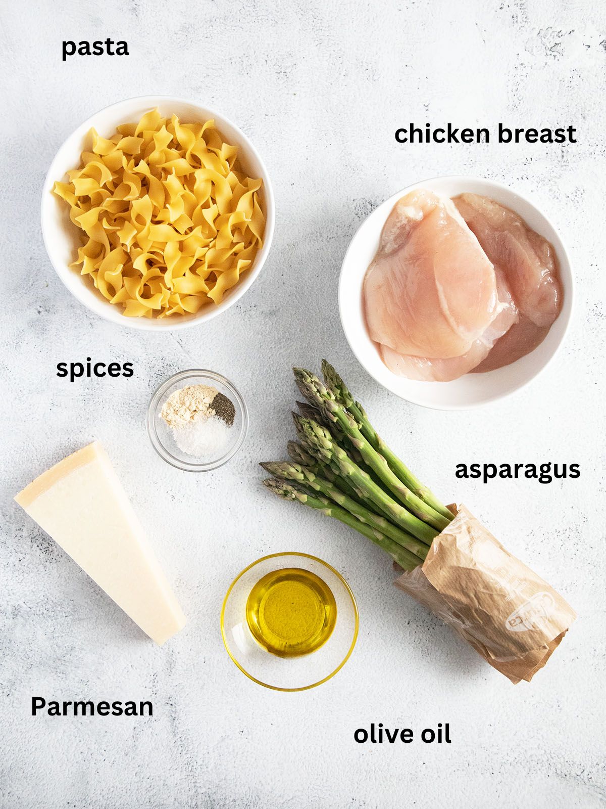 asparagus spears, parmesan, olive oil, pasta and chicken breast in bowls.